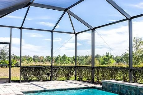 A screened-in patio overlooking a pool and lush greenery under a clear blue sky.