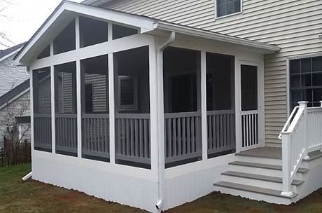 A white screened-in porch with a gabled roof and gray stairs attached to the back of a beige vinyl-sided house.