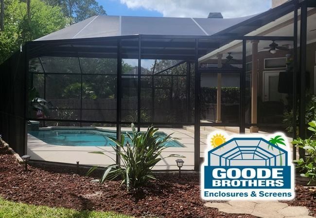 A black screened pool enclosure in a backyard setting, featuring a logo for Goode Brothers Enclosures & Screens.
