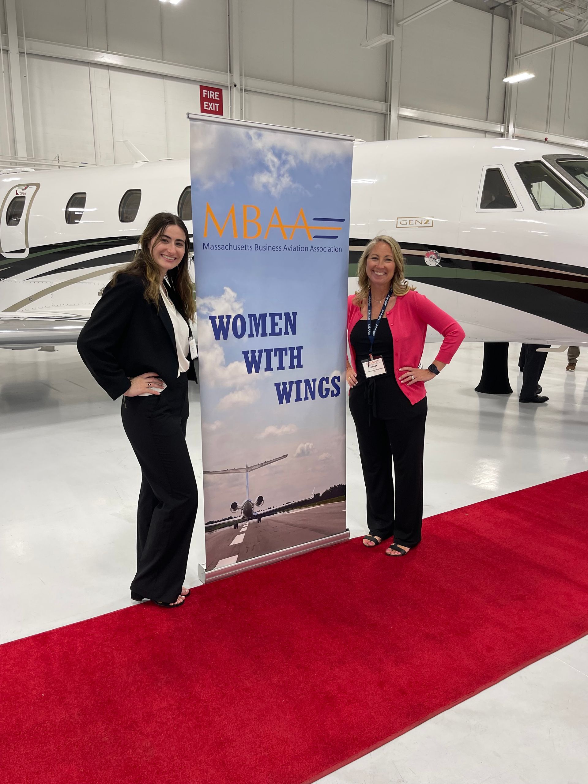 Two women standing next to a sign that says women with wings