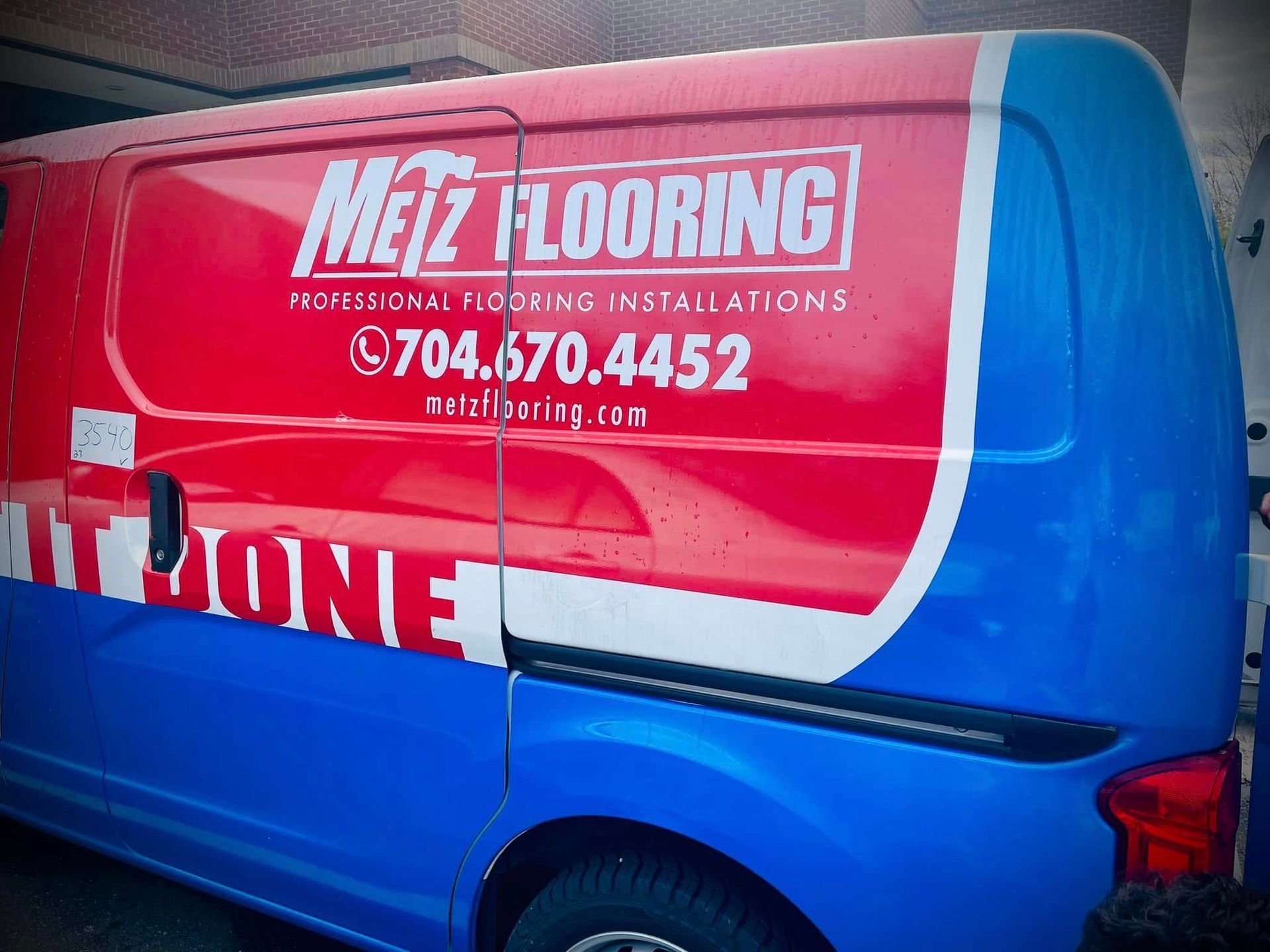 Red, white, and blue Metz Flooring van with company name, phone number, and website displayed on its side.