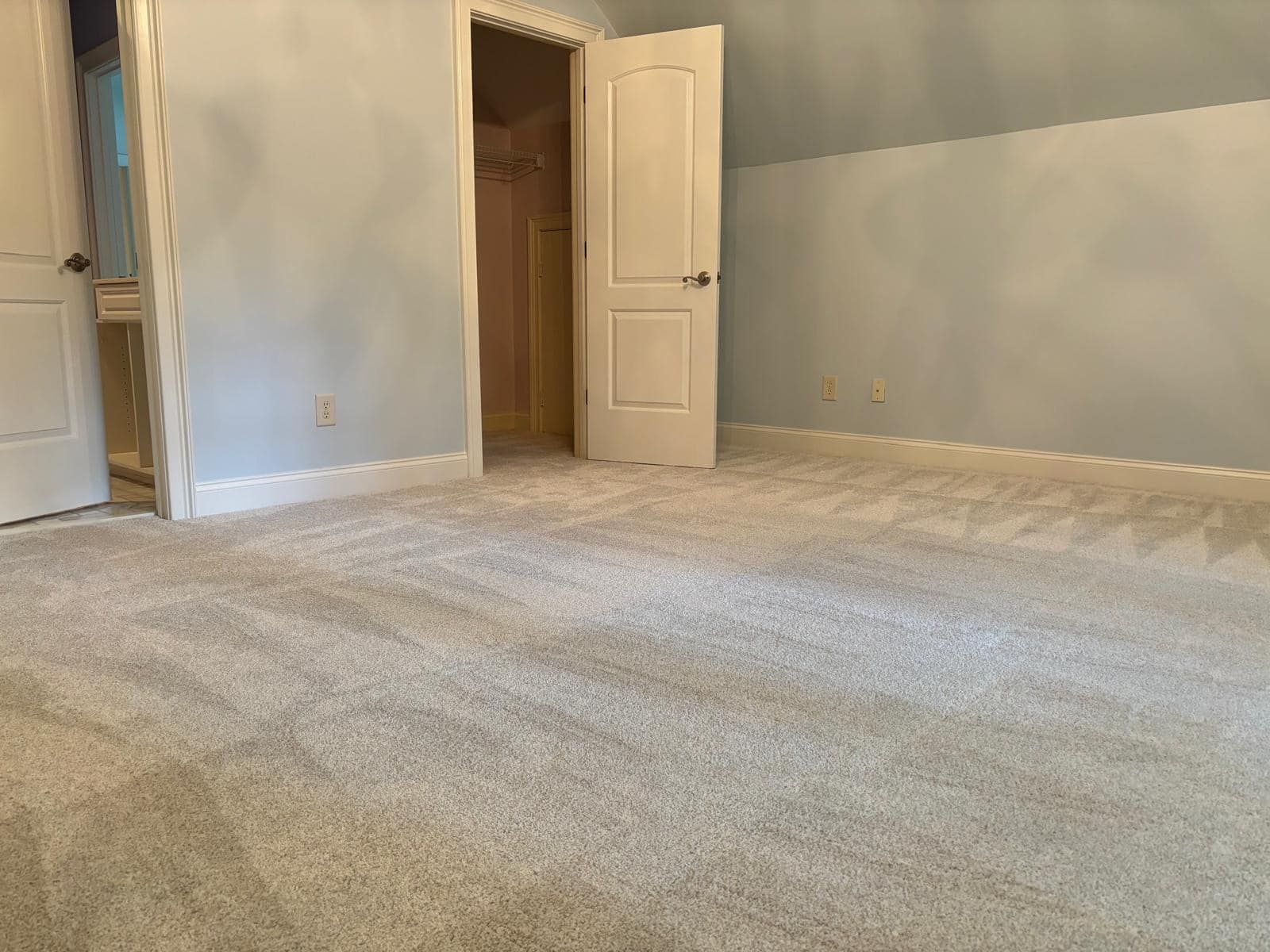 A bedroom with light blue walls, white doors, and beige carpet. One door is open leading to a closet.