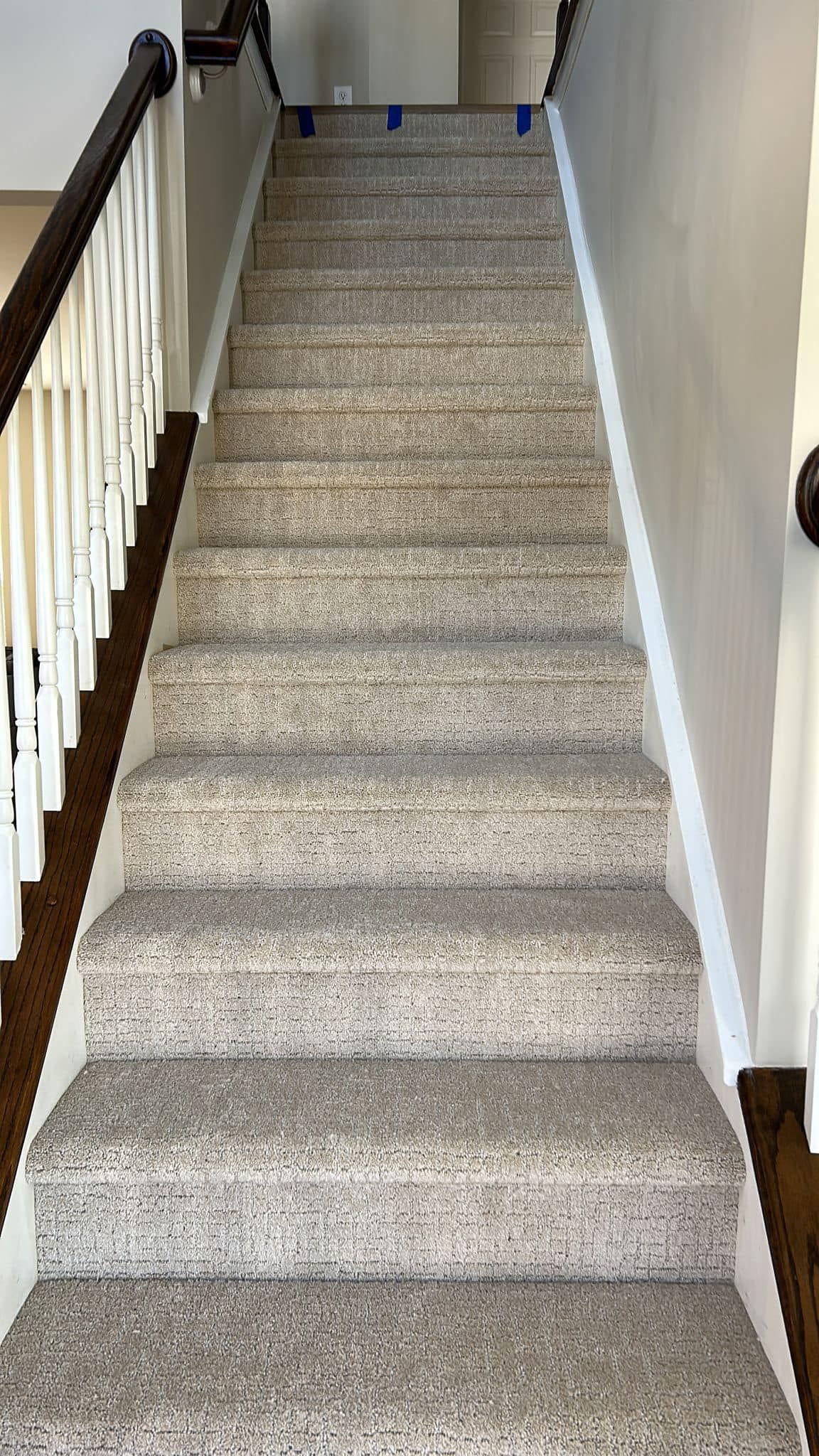 Staircase with carpeted steps, dark wood handrail and white spindles on the left. Gray walls, the stairs lead upwards.