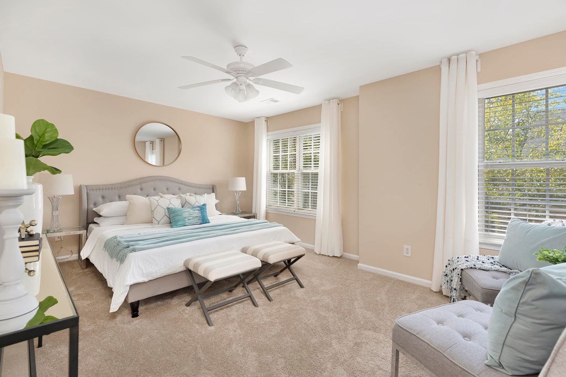Bedroom with a bed, two windows, seating area, and neutral color scheme.