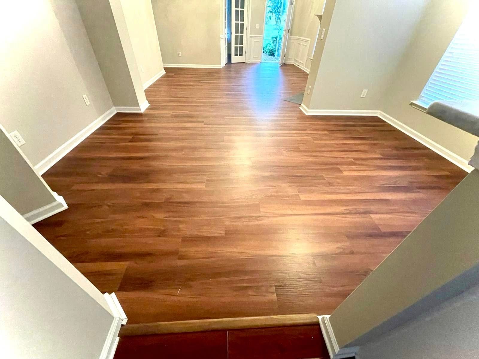 View from a staircase landing into a home with dark wood-look flooring, light gray walls, and a doorway at the far end.