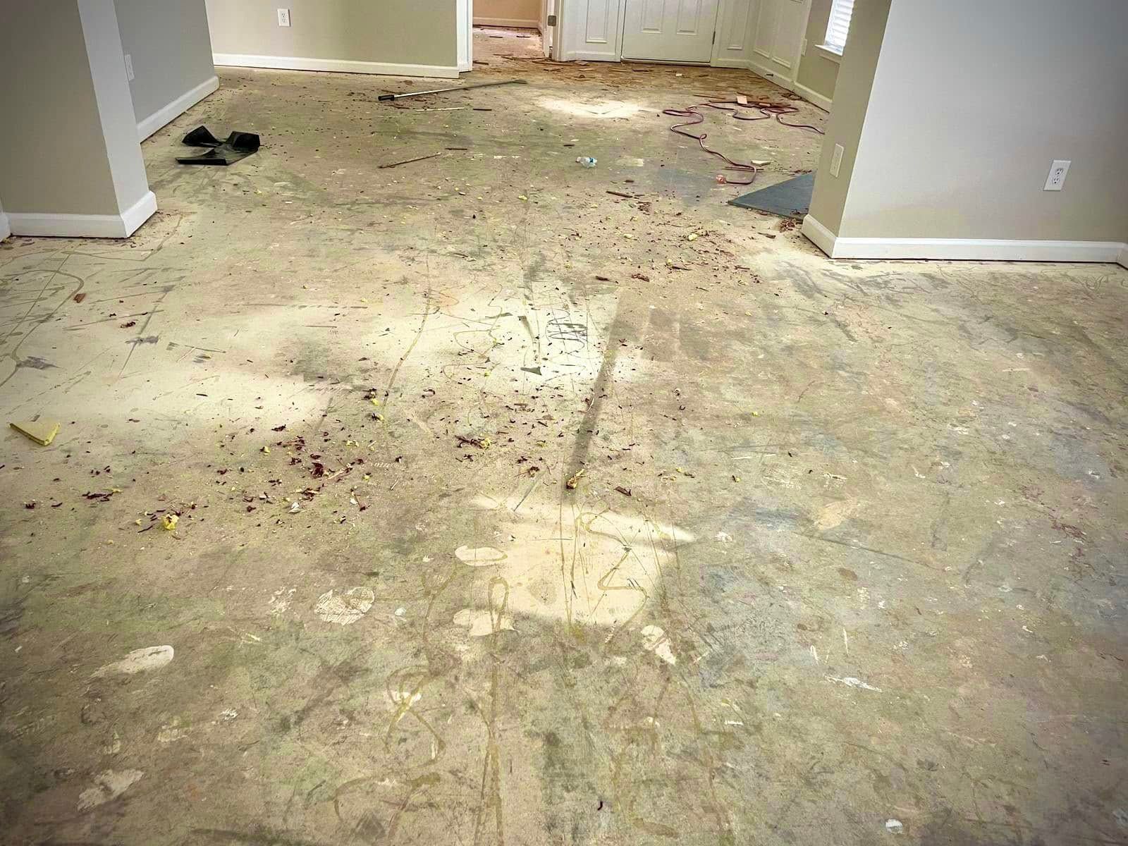 A concrete floor covered in debris, with visible markings and stains, in an empty room with painted walls.