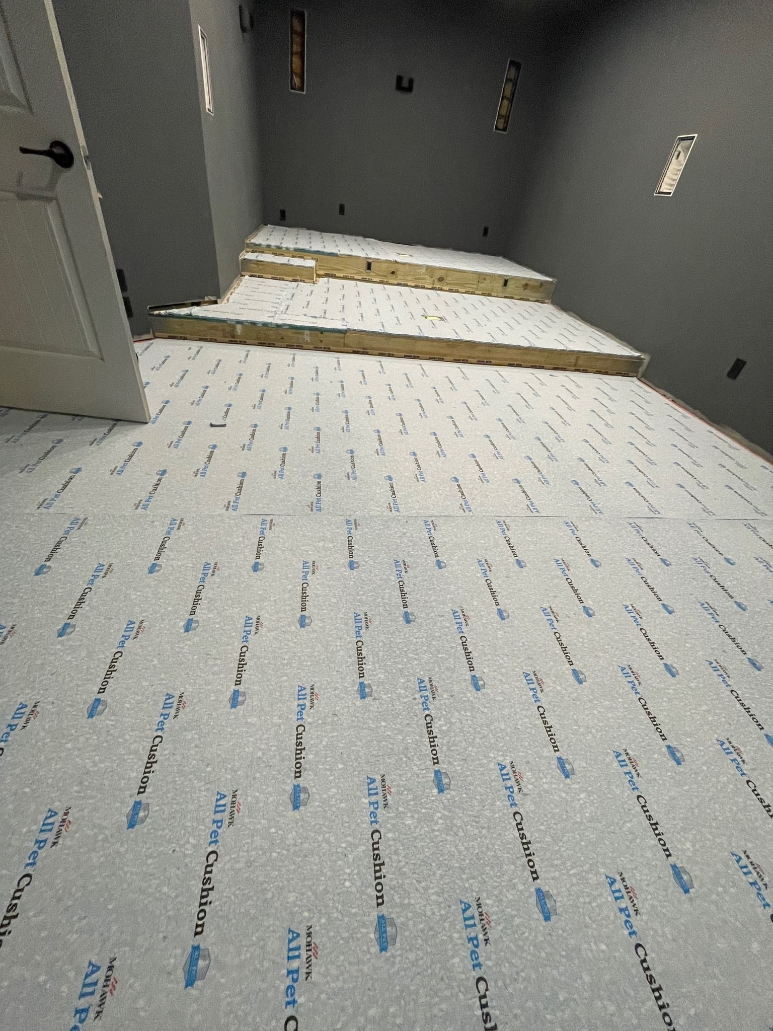 Room interior with white underlayment on the floor and steps. Insulation covers the elevated step platform.