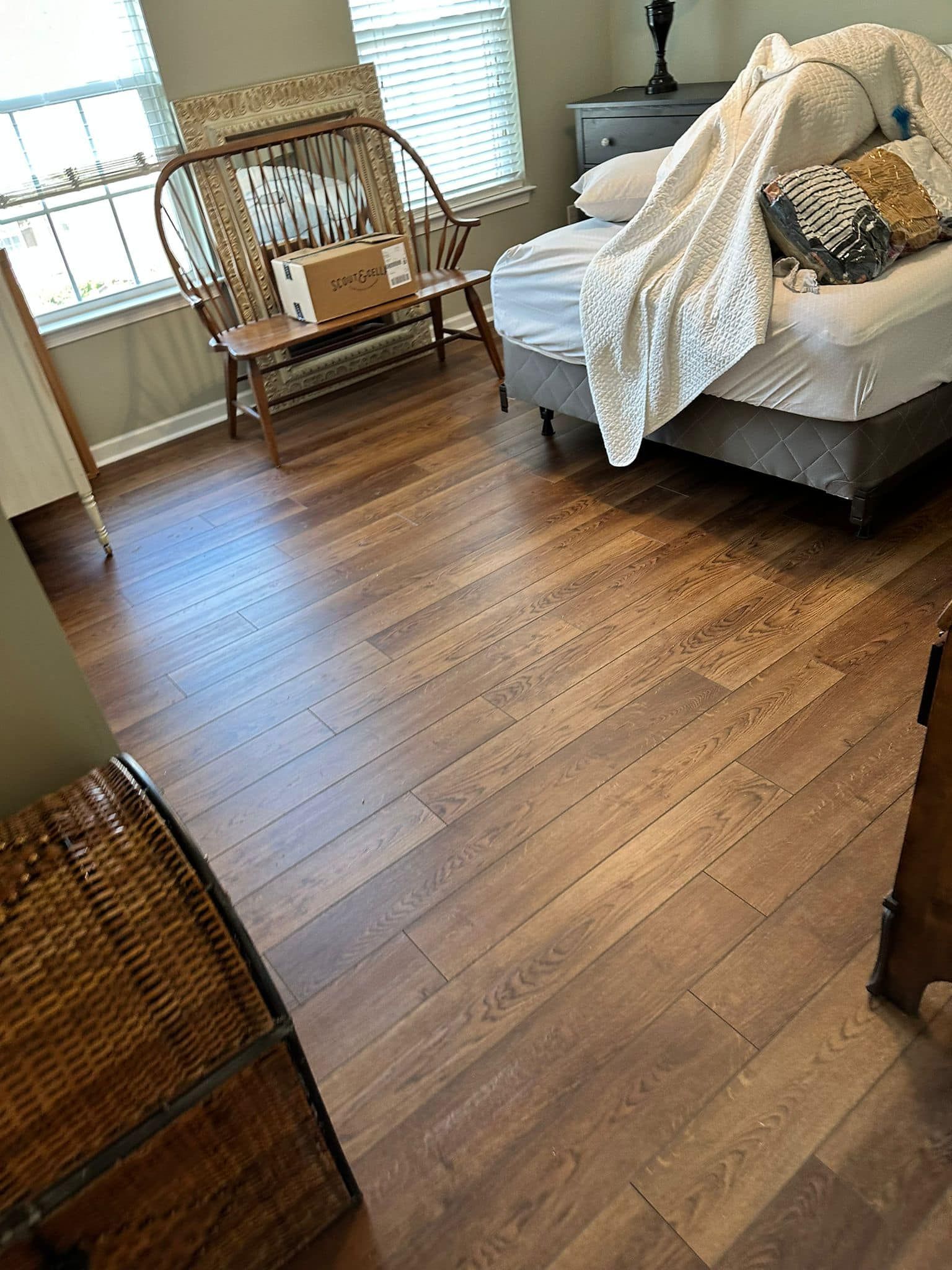 Hardwood floor in a bedroom with a bed, a chair, and a chest. The room has two windows with white blinds.