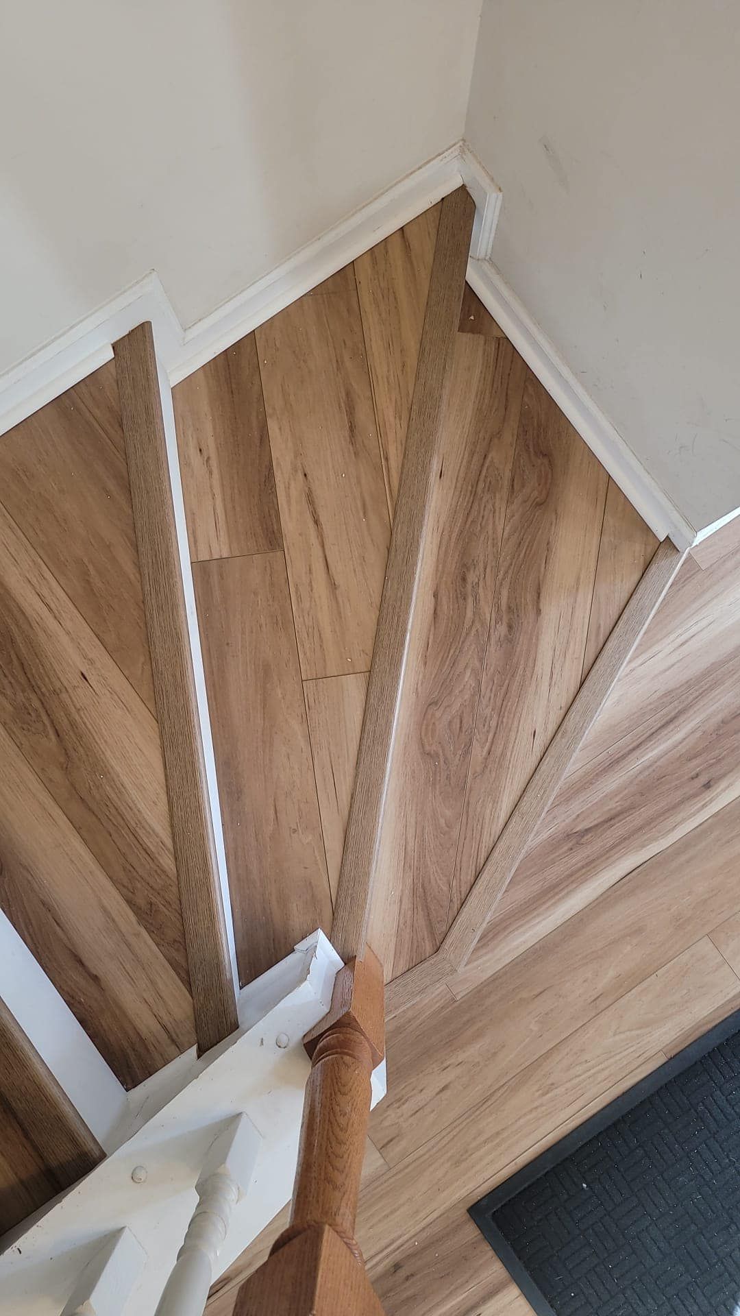 Looking down at a wooden, winding staircase. The stairs and landing have light brown wood-look flooring.