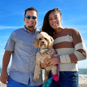 A man and woman holding a small dog on the beach