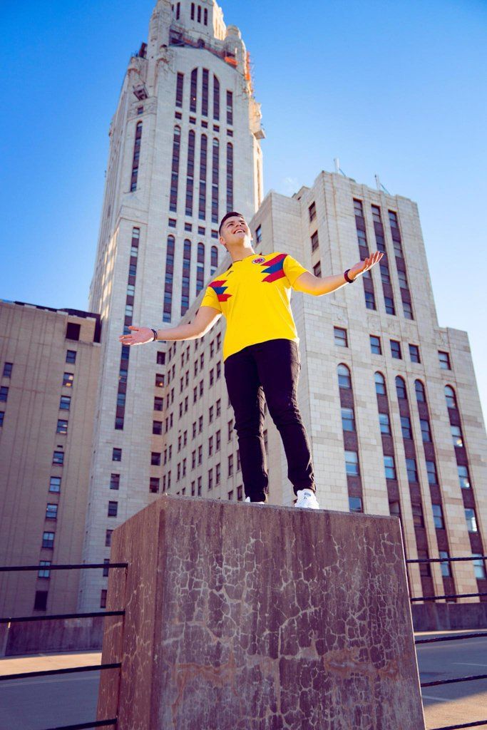 A man in a yellow shirt is standing on a ledge in front of a tall building