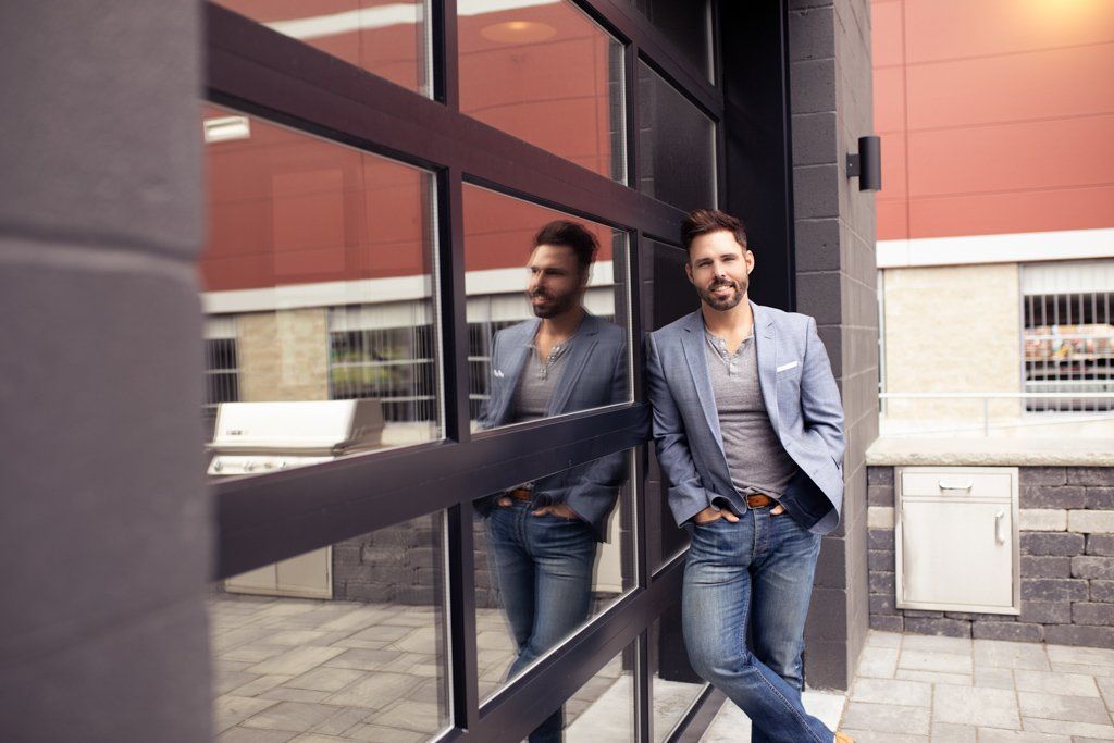 A man leaning against a building with his reflection in the window