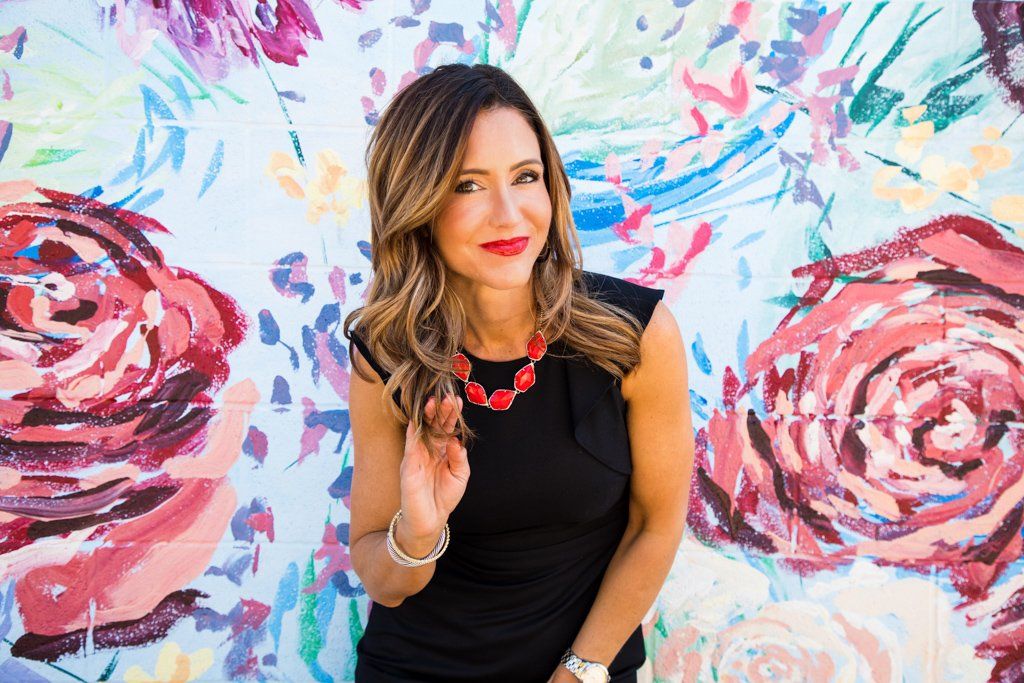 A woman in a black dress is standing in front of a wall with flowers painted on it