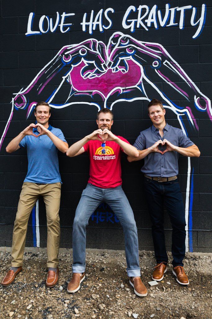 Three men are standing in front of a mural that says love has gravity