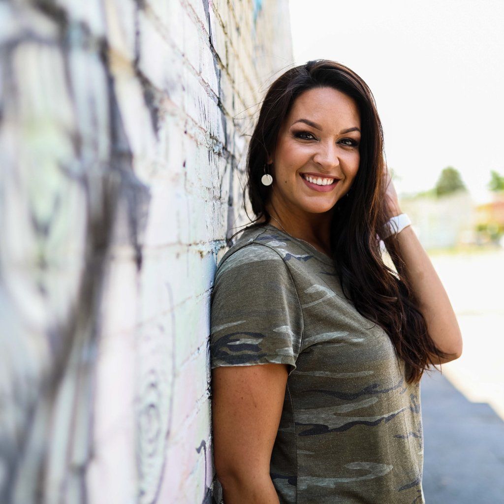 A woman is leaning against a brick wall and smiling