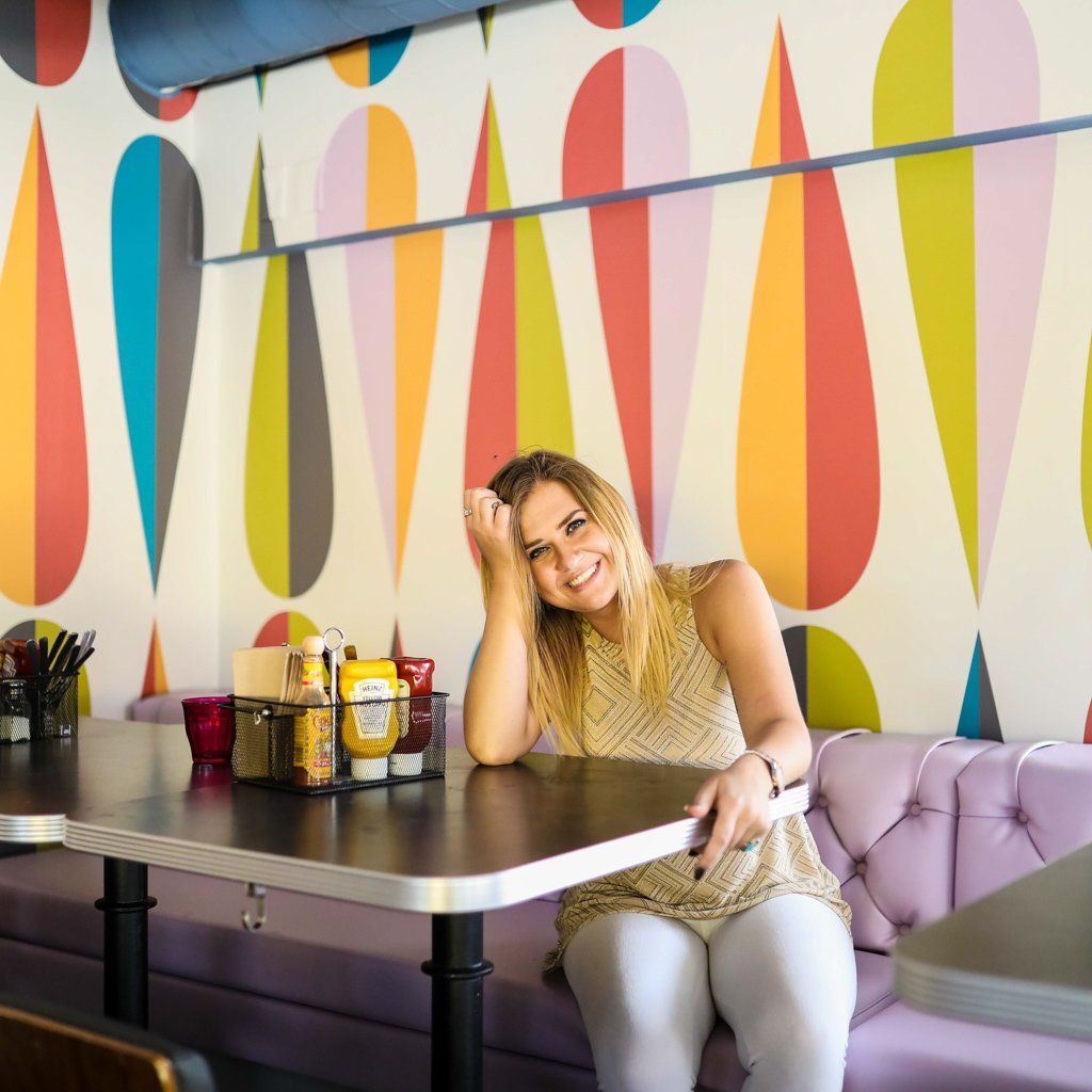 A woman sits at a table in front of a colorful wall