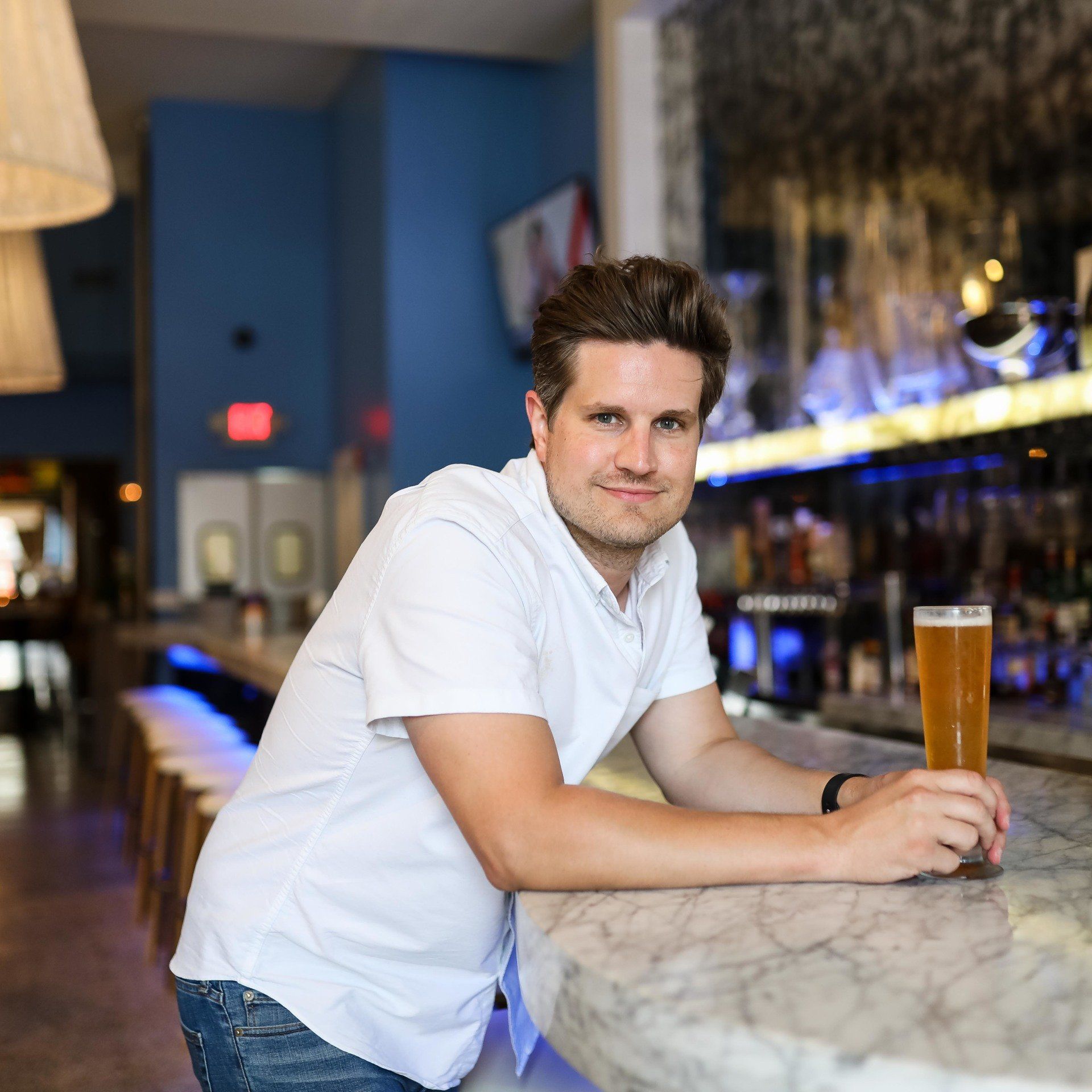 A man sits at a bar holding a glass of beer