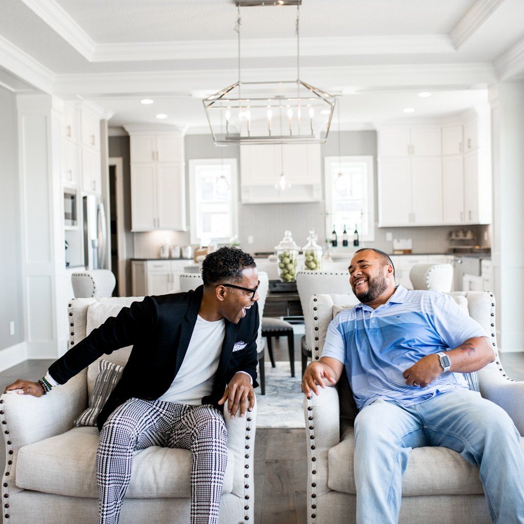 Two men are sitting on a couch in a living room laughing
