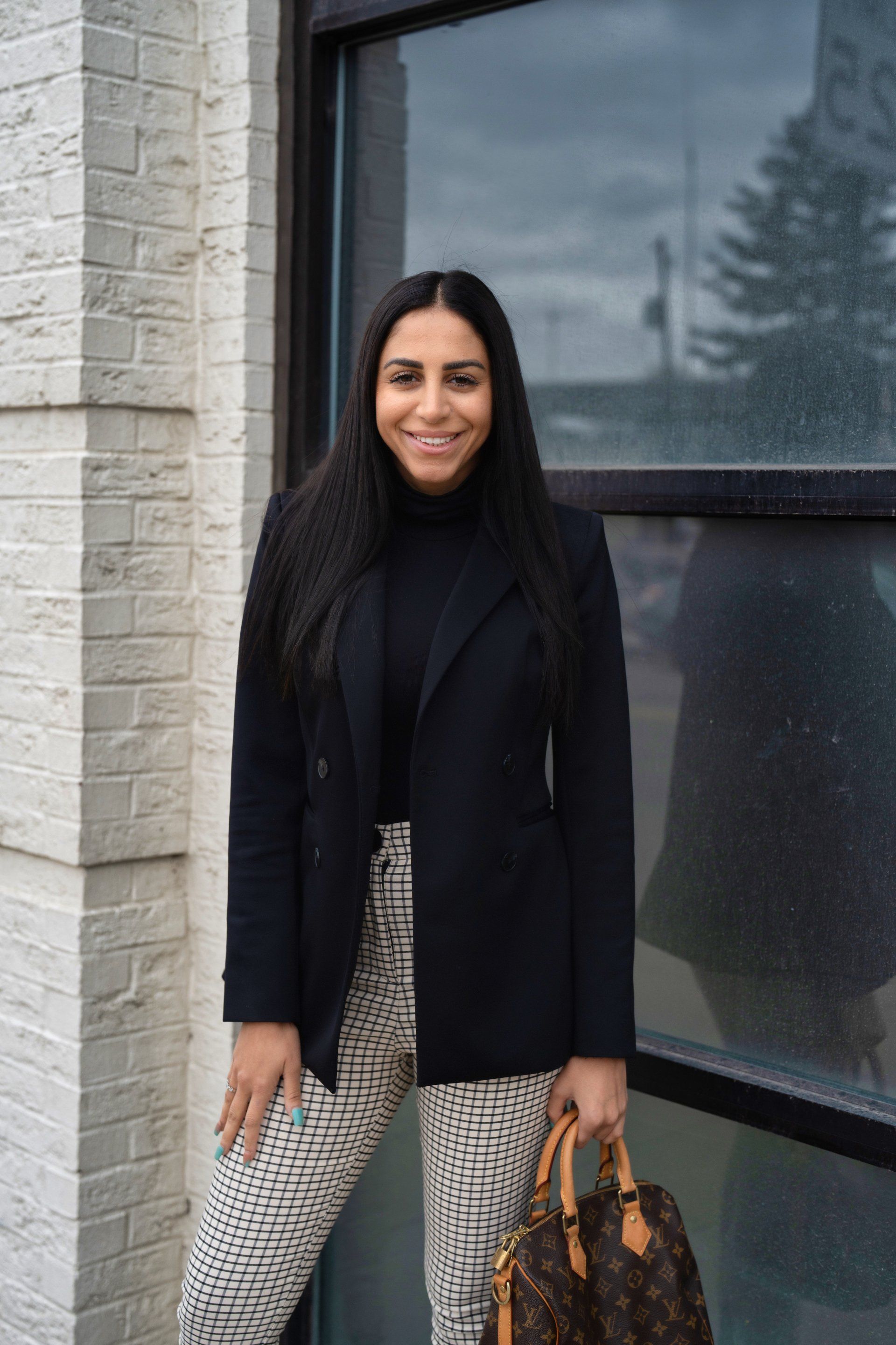 A woman in a black jacket and white pants is holding a louis vuitton purse