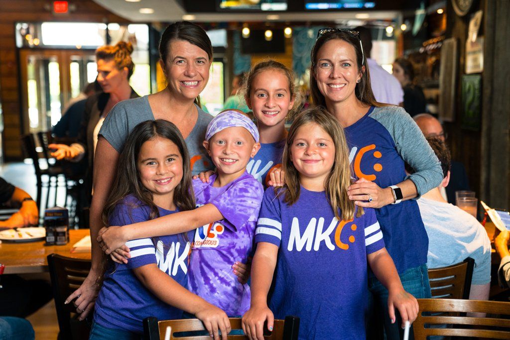 A group of girls wearing mkc shirts pose for a picture