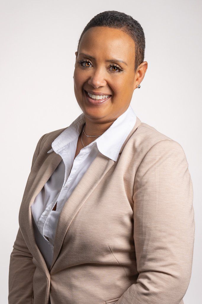 A woman in a tan jacket and white shirt is smiling for the camera.