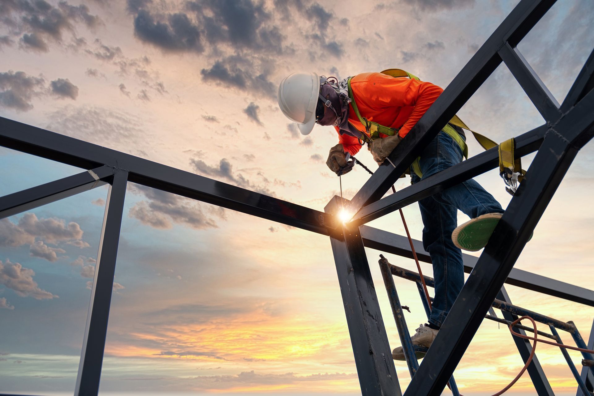 Construction worker welding metal beams at sunset