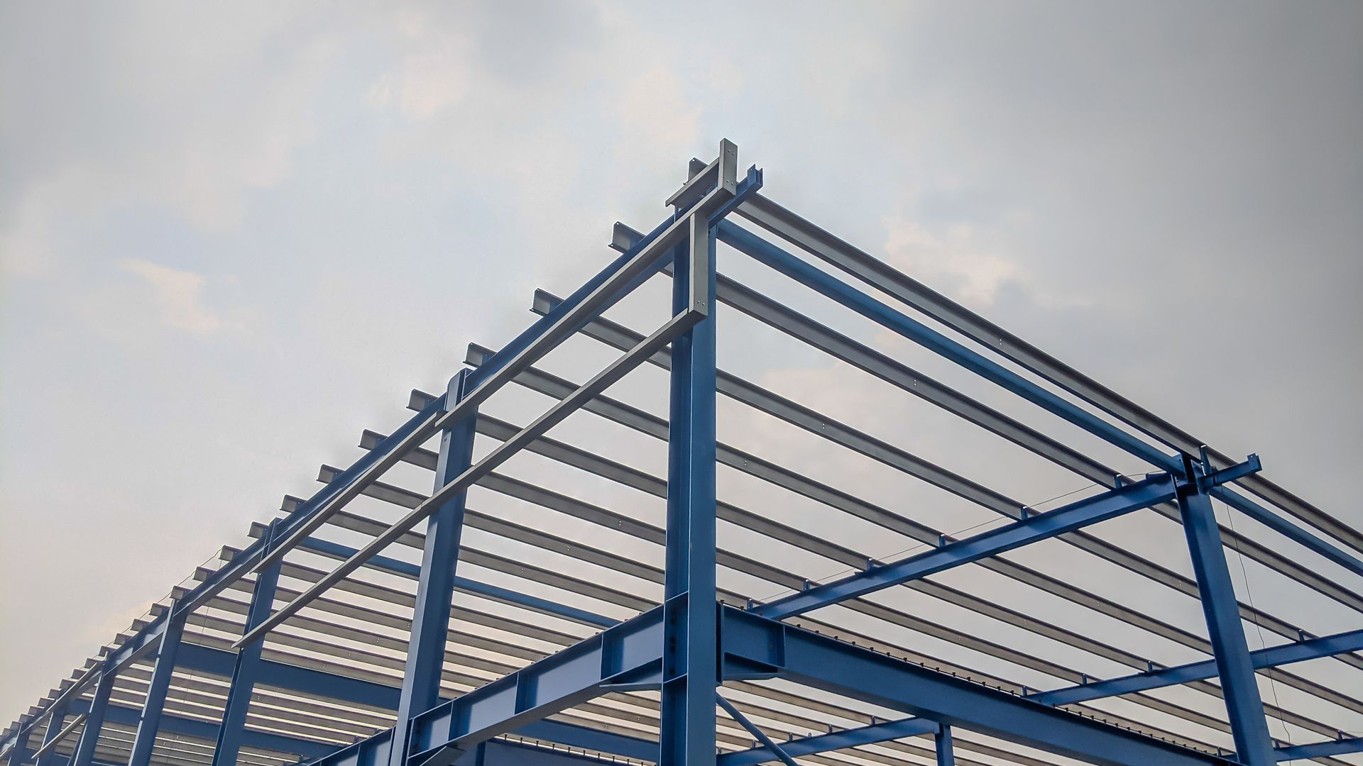 Blue steel frame of a building under construction against a cloudy sky