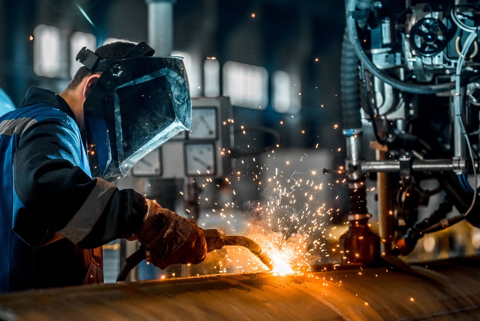 Welder wearing protective gear, welding a metal pipe in an industrial setting, with sparks flying