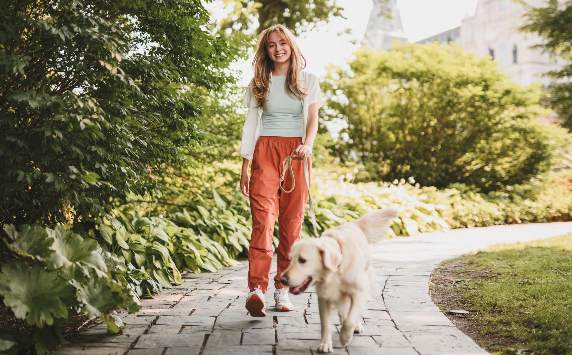 Woman walking golden retriever on a paved path in a park; sunny day.