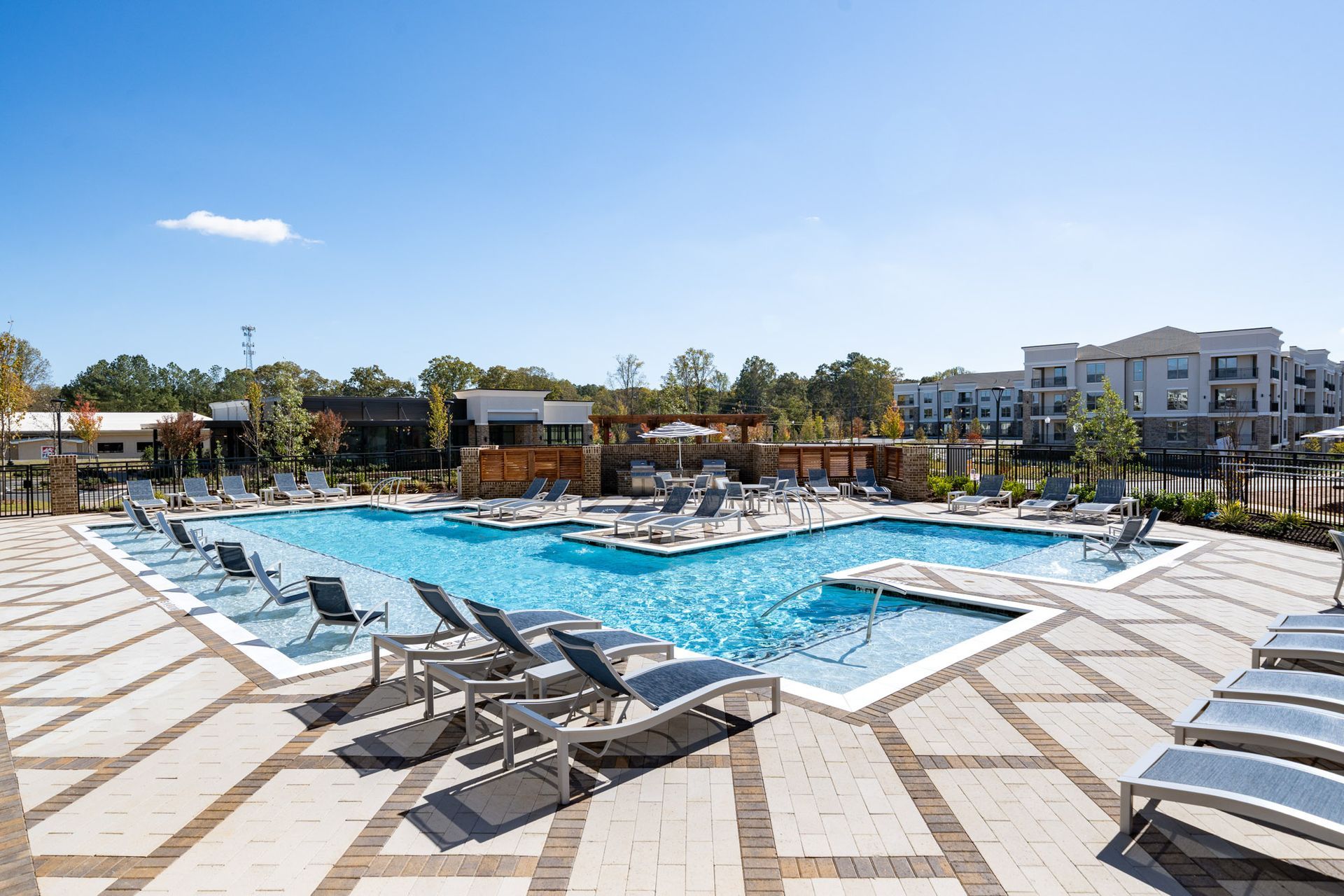Pool with lounge chairs on a sunny day. Apartment buildings in background.