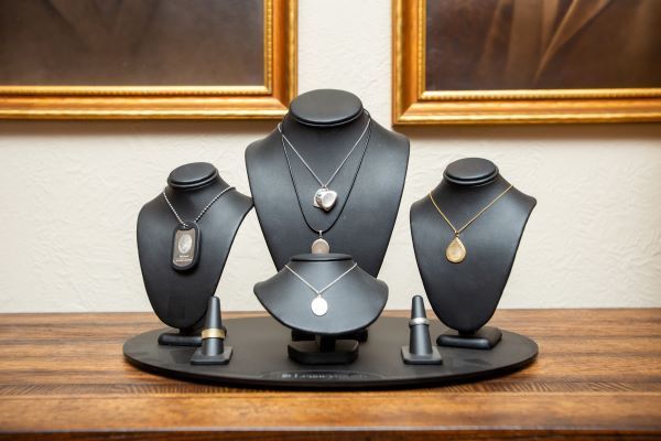 Jewelry display featuring five necklaces on black busts and two rings, arranged on a round black stand on a wooden surface.