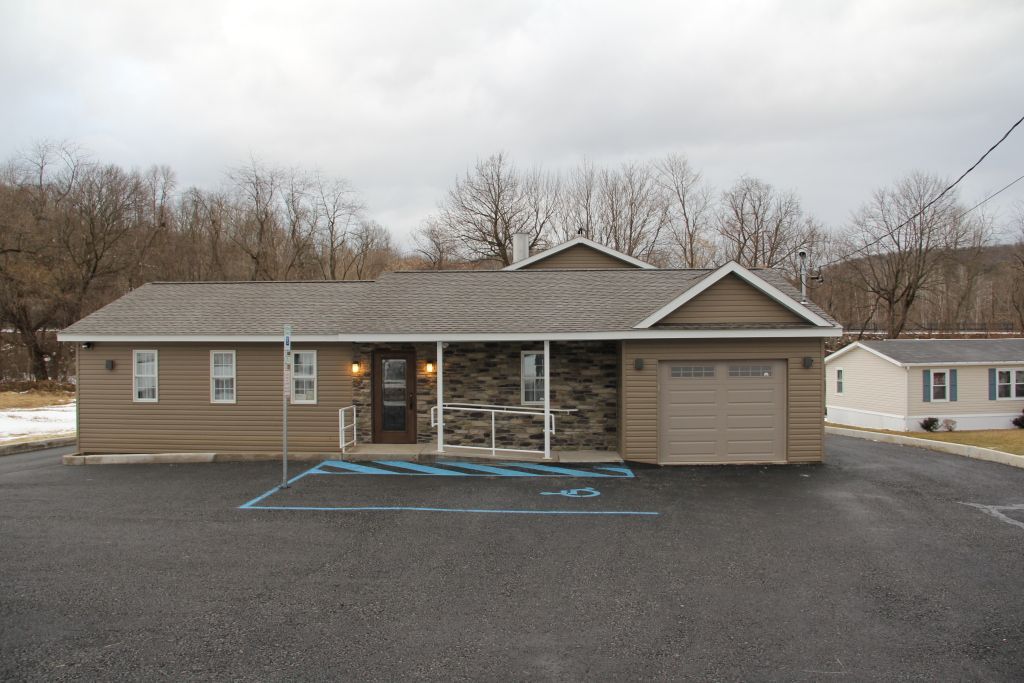 A one-story building with brown siding and a stone facade, with a garage door on the right. The building has a dark paved parking lot in front.
