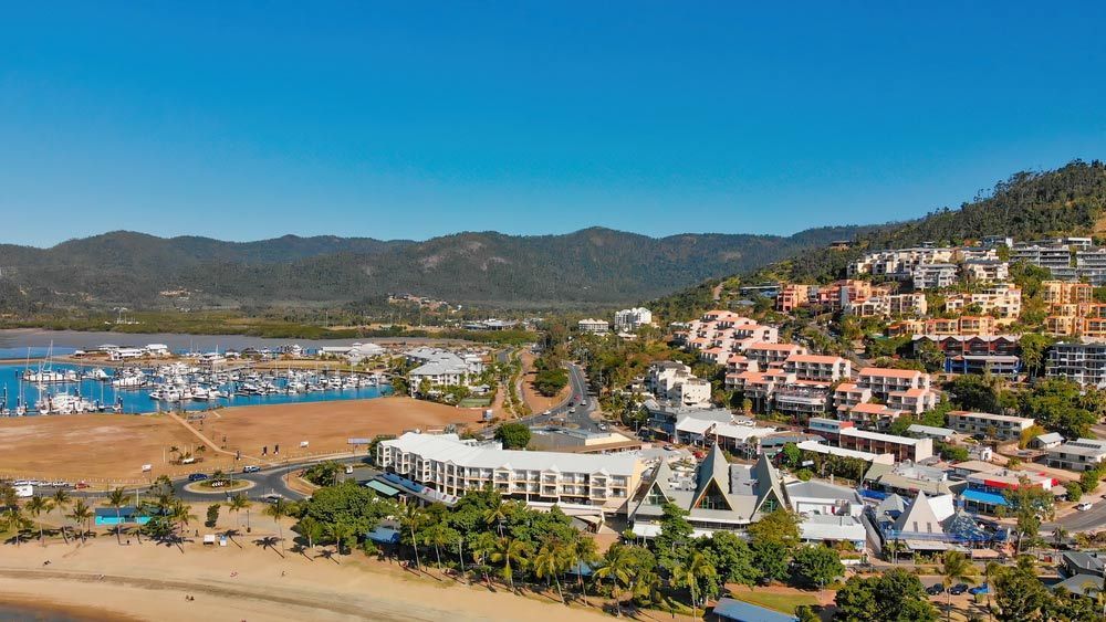 An Aerial View Of A City With A Beach And Mountains In The Background — Dieselflash Whitsundays in Airlie Beach, QLD