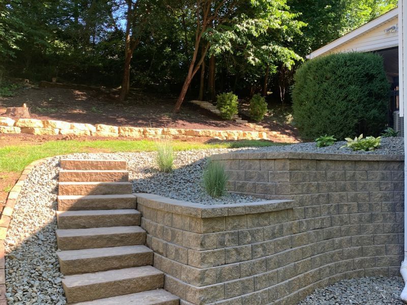 Stone steps lead up a hillside with retaining walls made of tan blocks and green shrubs.