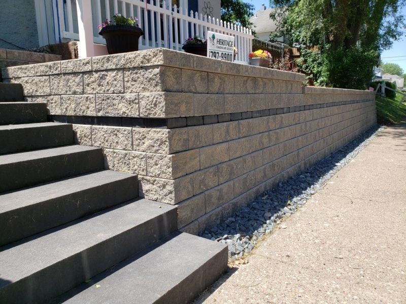 A beige and dark grey block retaining wall with matching steps leading to a house. Black decorative strip runs across the wall.