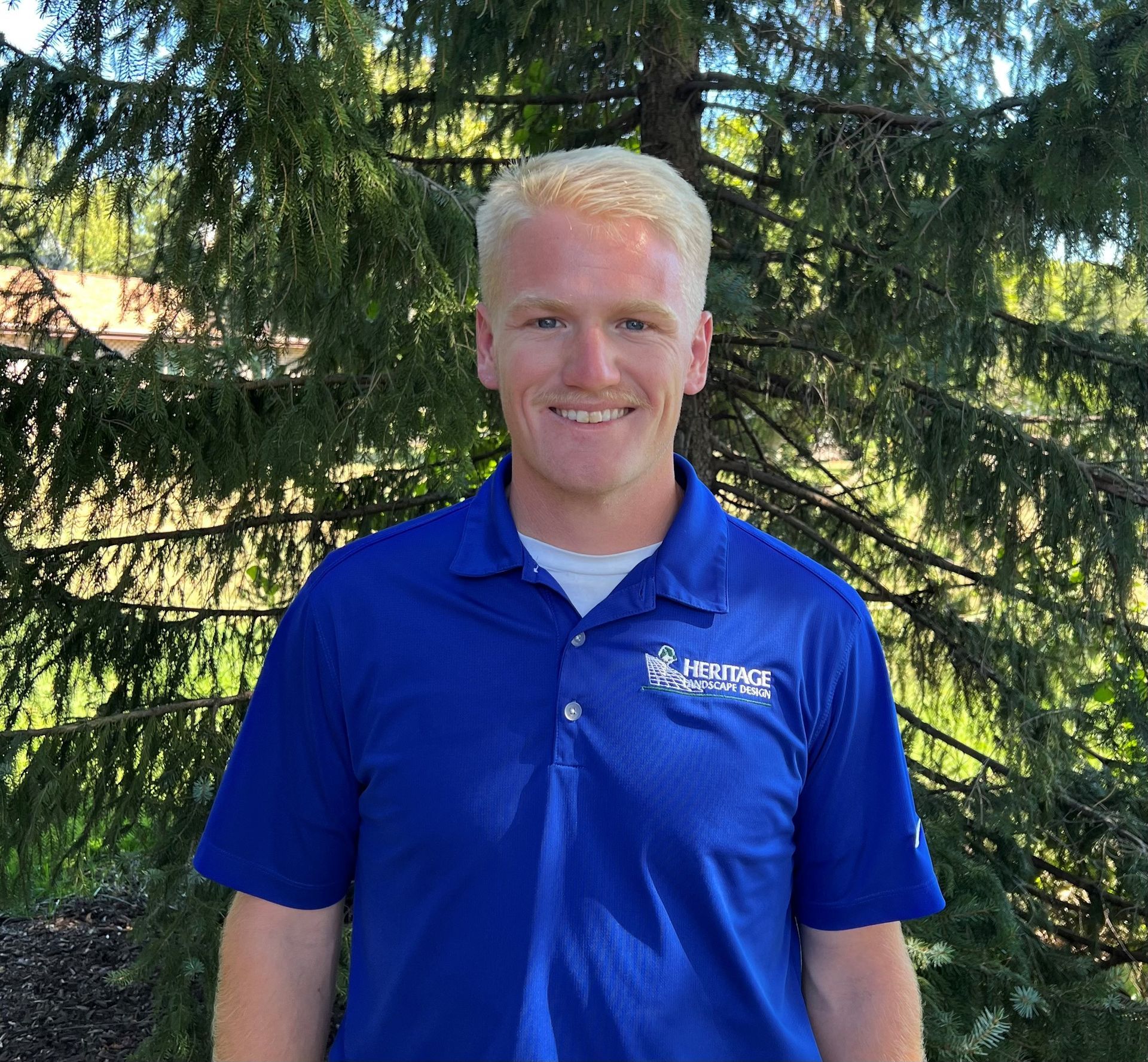 A man in a blue shirt is standing in front of trees.