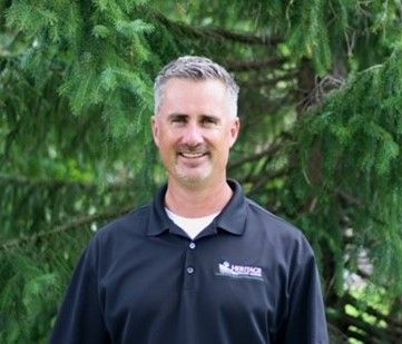 A man in a black shirt is standing in front of a tree.