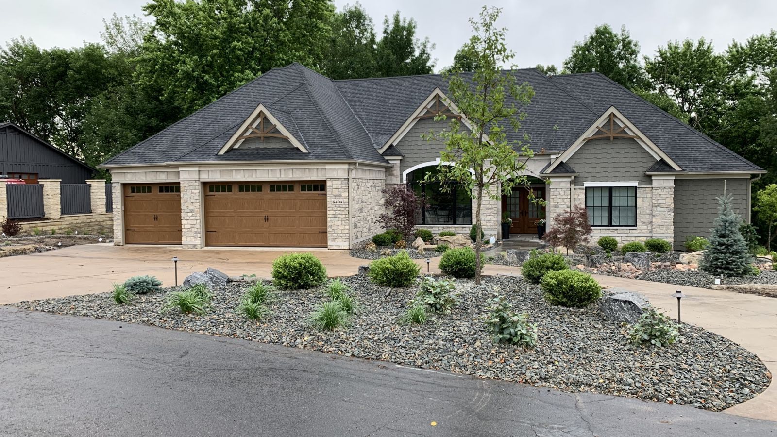 A single-story home with a gray roof and brown garage doors. The house features light-colored brick and a stone landscaping.