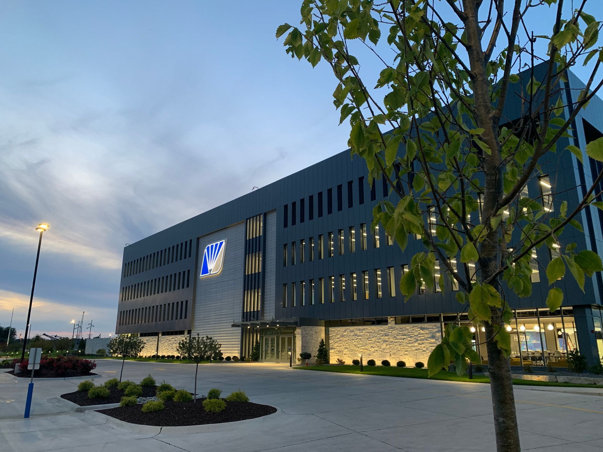 Modern gray office building with the emblem of the Polish Football Association, illuminated at dusk, with a tree in the foreground.