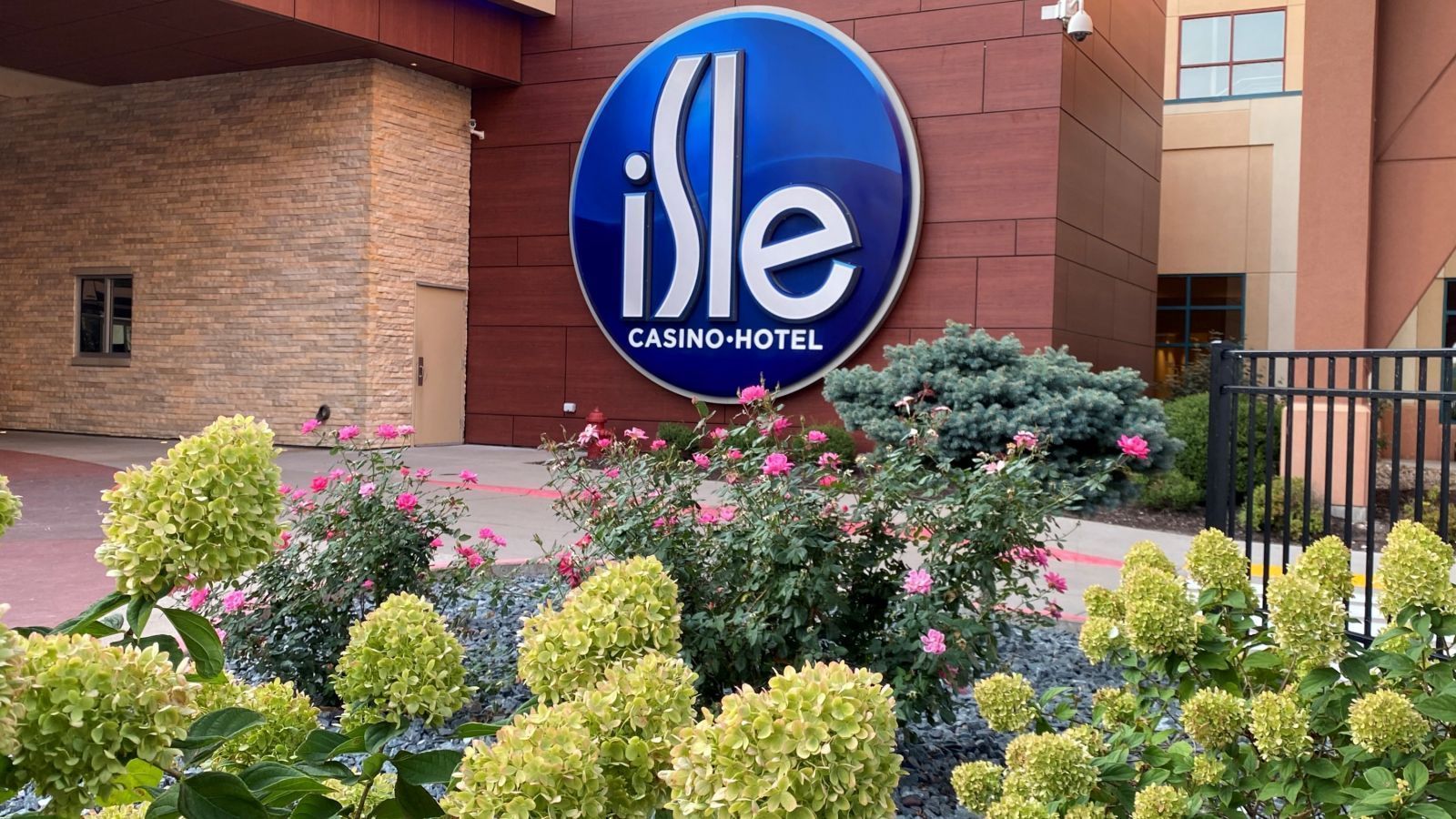 Isle Casino Hotel entrance with a large blue sign, brick and tan building, surrounded by flowers.