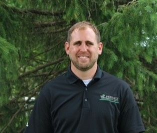 A man in a black shirt is standing in front of a tree.