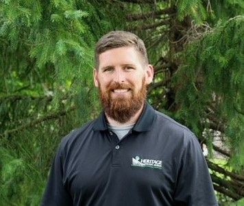 A man with a beard is standing in front of a tree.