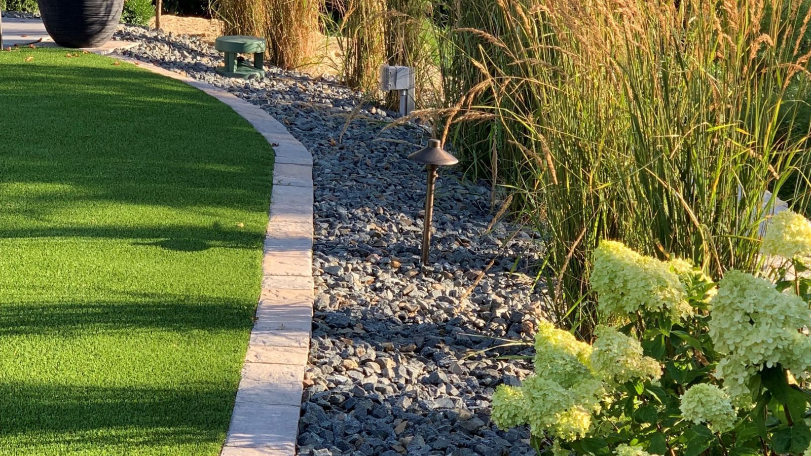 A landscaped garden bed with gray gravel, tall grasses, and a border next to artificial green grass.