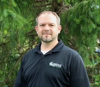 A man in a black shirt is standing in front of a tree.