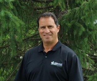 A man in a black shirt is standing in front of a tree.