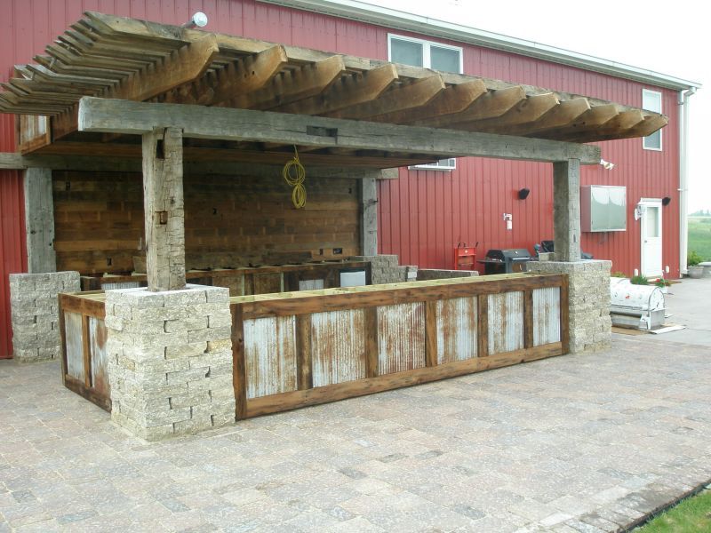 Outdoor bar with a wood and stone structure, featuring a pergola roof and a brick patio.