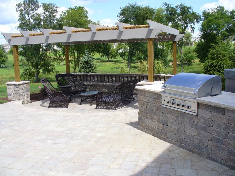 Outdoor patio with a pergola, grill, seating area, and brick walls in a park-like setting.