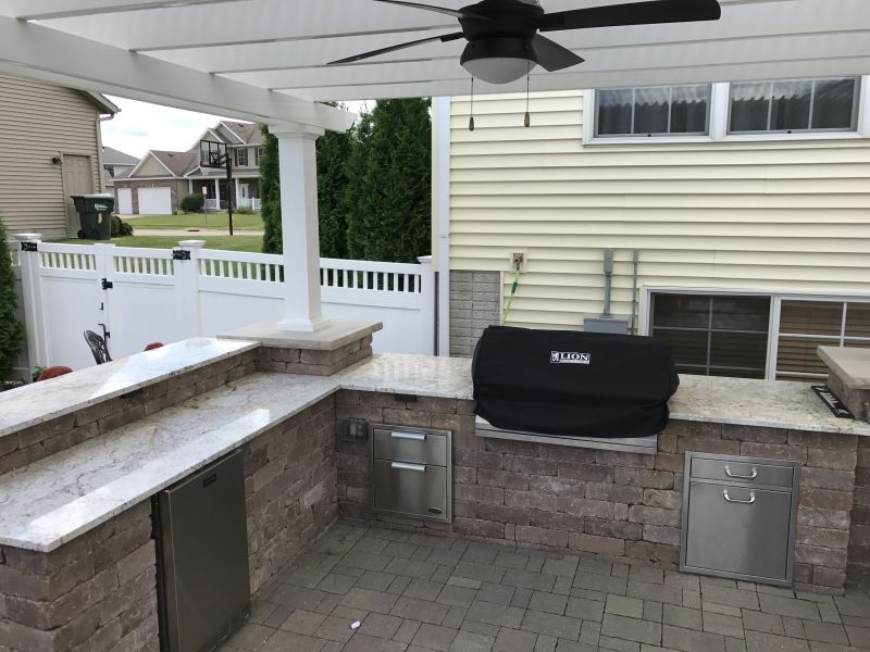 Outdoor kitchen with a built-in grill, refrigerator, and counter space, covered by a pergola.