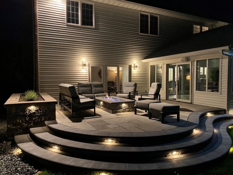 A patio with furniture and a fire pit is lit up at night.