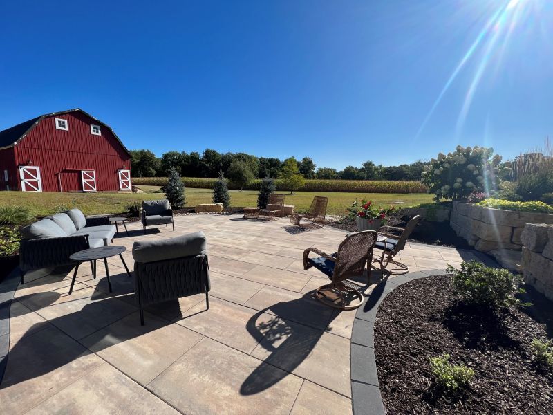 Outdoor patio with seating overlooking a red barn and a cornfield under a sunny, blue sky.
